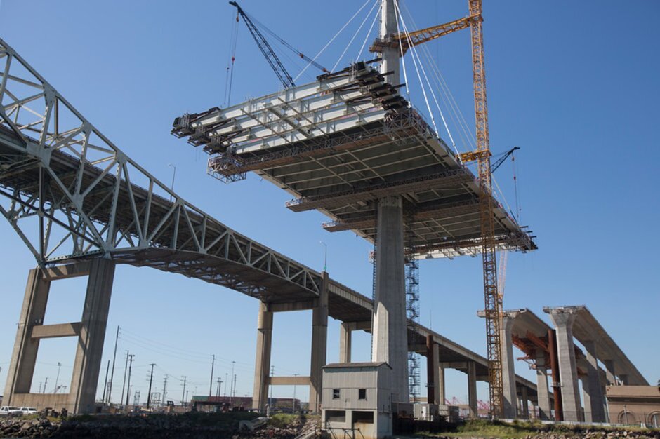 Bridge construction project with cranes installing a large steel span over concrete support columns.