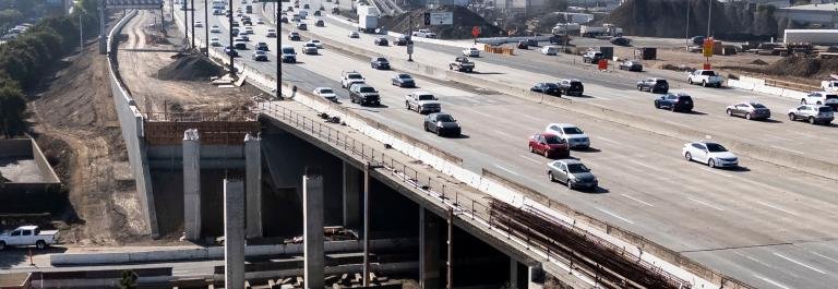 Highway infrastructure project with bridge construction and active traffic, representing federal infrastructure and transportation programs.