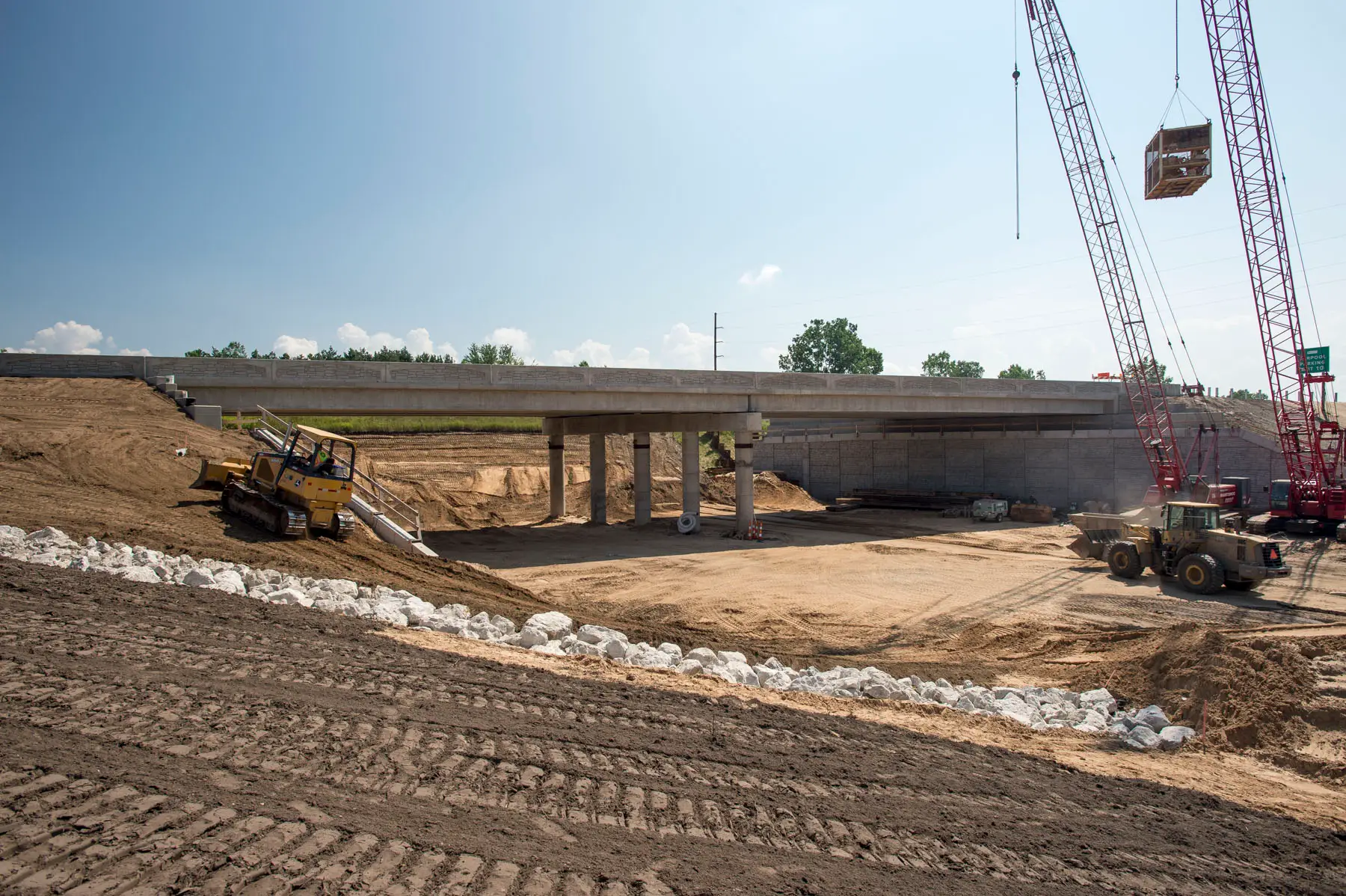 Heavy equipment performs earthwork beneath a newly constructed highway overpass at the I-96 and M-231 interchange in Michigan.